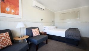 studio bedroom with double bed and two chairs with funky cushions in Bathurst