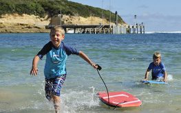 port campbell children playing at beach with body boards