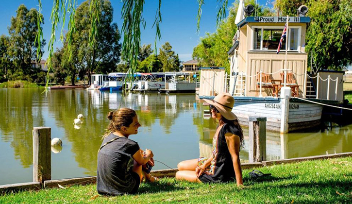 two females sitting next to Lake Mulwala having a chat with boats in the background