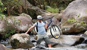 Man carrying mountain bike through rock pools in the Atherton Tablelands