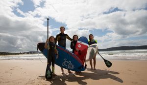 Family standing with stand up paddle board on the beach in Umina Beach