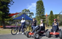 2 adults on bicycles and 2 kids riding Pedal go-karts inside NRMA Ocean Beach Holiday Resort
