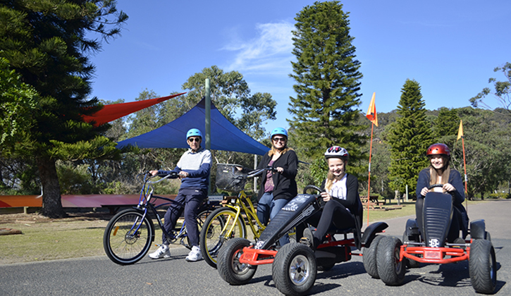 2 adults on bicycles and 2 kids riding Pedal go-karts inside NRMA Ocean Beach Holiday Resort